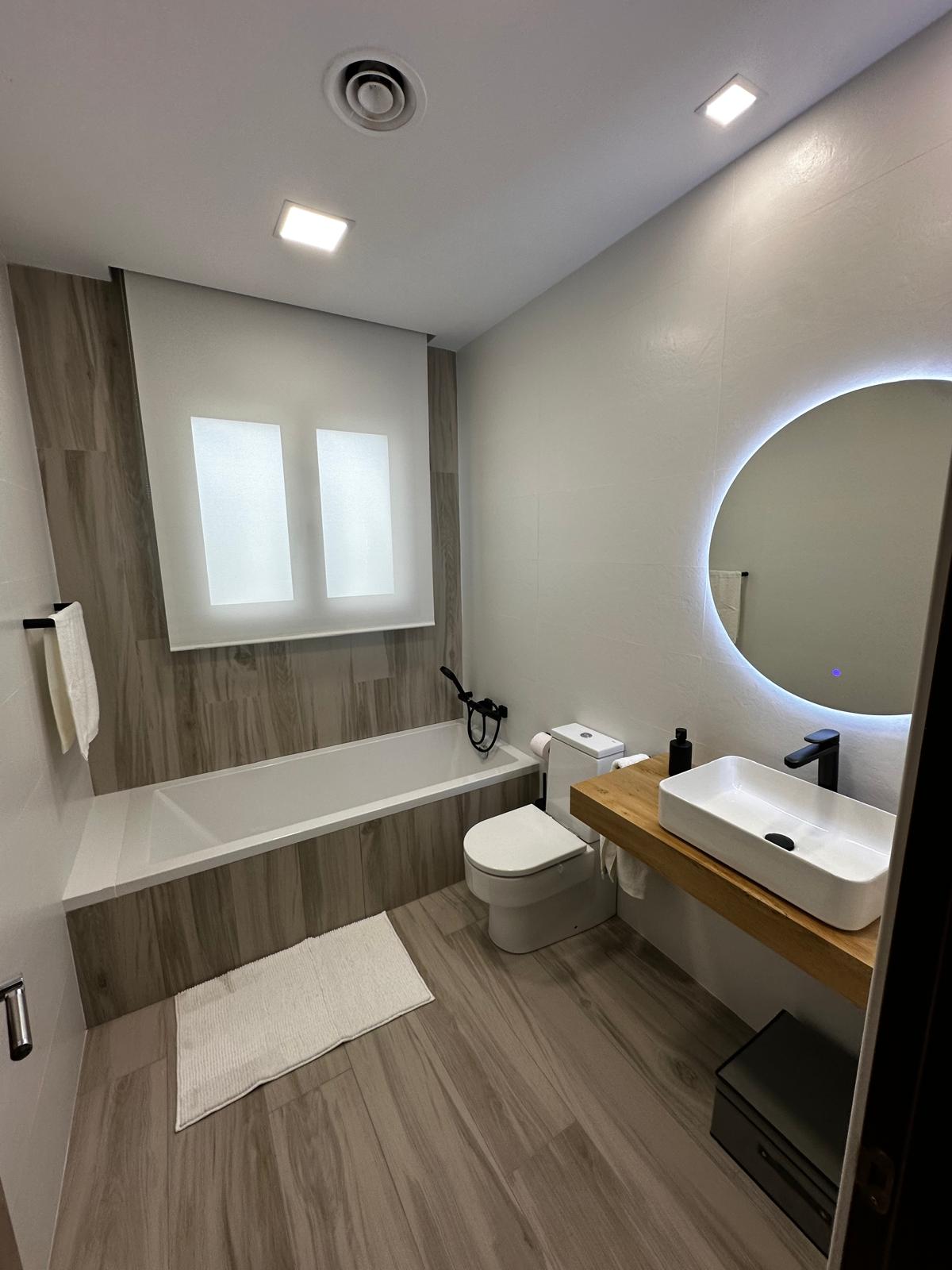 Baño terminado con espejo redondo y mueble de madera